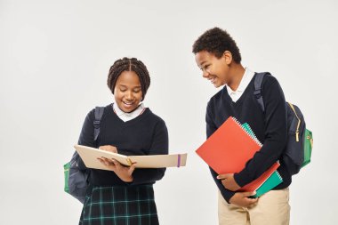 Okul üniformalı mutlu Afro-Amerikan çocukları ellerinde ders kitapları ve gri arka planda duruyorlar.