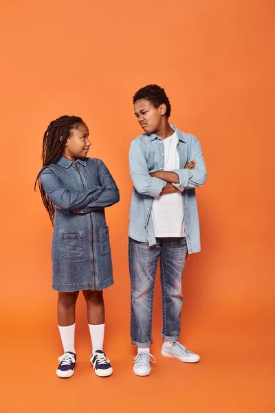 stock image african american children in casual denim attire posing with folded arms on orange background
