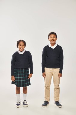 Üniformalı Afro-Amerikan okul öğrencileri gri arka planda birlikte poz veriyor ve kameraya gülümsüyor.