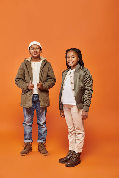 Радостная африканская девушка и мальчик в теплых нарядах позируют вместе и улыбаются в камеру