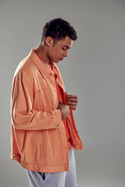 Gri duvarda duran şeftali rengi gömlekli yakışıklı adam, kusursuz moda anlayışını sergiliyor.