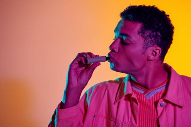 Elektronik sigaralı Afro-Amerikan bir adam ışıklandırmalı, buharlaştırmalı renkli arka plana karşı.
