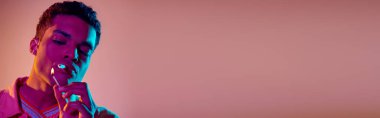 Afro-Amerikalı bir adam, pembe arka planda mavi neon ışıkları altında kibritle sigara yakıyor.