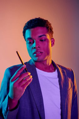 Pembe arka planda mavi neon ışıkların altında sigara tutan yakışıklı Afro-Amerikan bir adam.