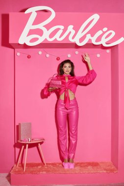 KYIV, UKRAINE - 14 Temmuz 2023: Kırpılmış bluzlu ve pembe pantolonlu kadın gibi çekici bir bebek Barbie harflerinin yanında duruyor.