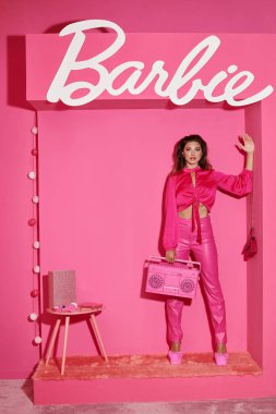 KYIV, UKRAINE - 14 Temmuz 2023: Pembe elbiseli güzel bir kadın retro müzik kutusunu tutuyor ve Barbie işareti yakınında el sallıyor.