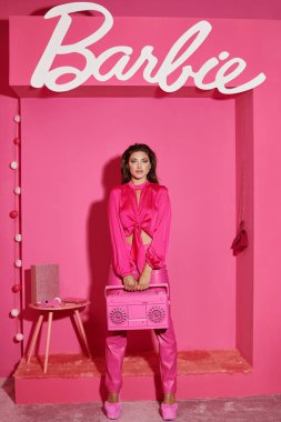 KYIV, UKRAINE - 14 Temmuz 2023: canlı giyinmiş güzel bir kadın pembe arka planda retro müzik kutusunu tutuyor, Barbie işareti