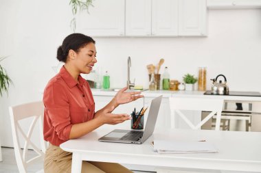 Mutlu Afro-Amerikan kadın beslenme uzmanı mutfaktan dizüstü bilgisayarına danışmanlık yapıyor.