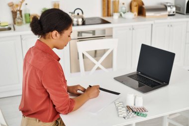 nutritionist writing prescription near different medication next to laptop with blank screen clipart