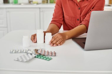 cropped view of african american dietitian near bottles with different medication on table clipart
