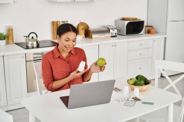 Afrika kökenli Amerikalı beslenme uzmanı internette diyet tavsiyesi verirken elinde elma ve takviyeler tutuyor.