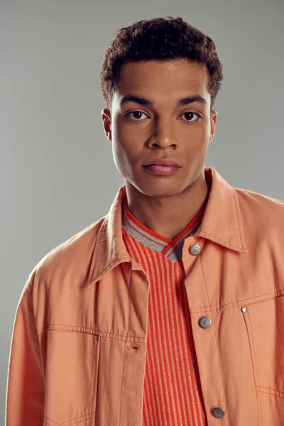 stock image young african american man in peach color shirt looking at camera on grey backdrop, gen z fashion