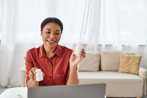 positive nutritionist showing bottles with different medication during online consultation on laptop