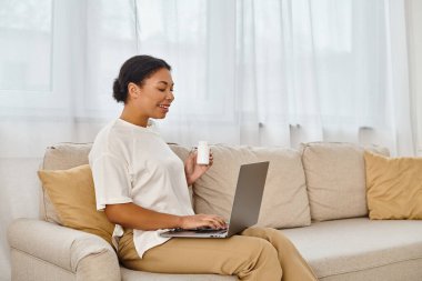 happy african american nutritionist with supplements giving dietary tip via laptop in living room clipart