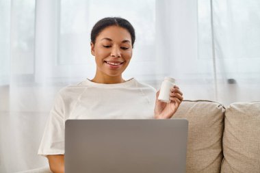 cheerful african american nutritionist with supplements giving dietary tip via laptop in living room clipart