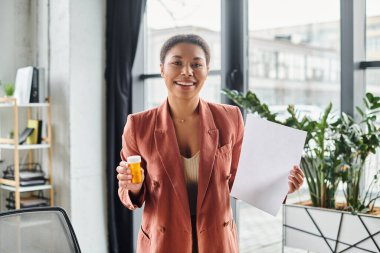 Mutlu Afro-Amerikan beslenme uzmanı fotokopi alanı ve takviyeli şişe gösteren bir kağıt gösteriyor.