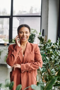 Neşeli Afro-Amerikan beslenme uzmanı yeşil ofisteki akıllı telefon aracılığıyla danışmanlık yapıyor.