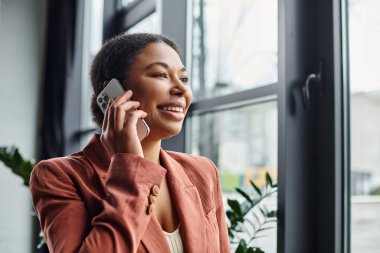 Mutlu Afro-Amerikan beslenme uzmanı yeşil ofisteki akıllı telefon aracılığıyla danışmanlık yapıyor.
