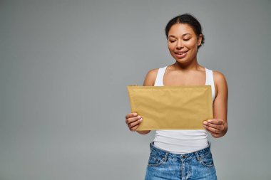 happy african american dietitian holding envelope containing a dietary plan on grey backdrop clipart