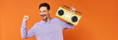 Mor kazaklı neşeli ve sakallı adam elinde turuncu arka planda retro boombox tutuyordu.