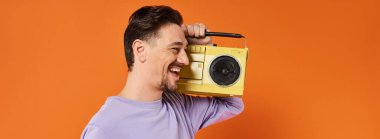 Mor kazaklı mutlu adamın flaması elinde teyp ve turuncu arka planda müzik dinliyor.
