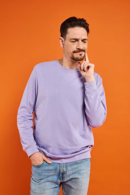 Mor kazaklı ve kot pantolonlu sakallı adam turuncu arka planda dişinde ağrıdan muzdarip.