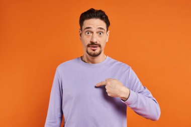 surprised bearded man in purple sweater with eyes wide open pointing at himself on orange background clipart
