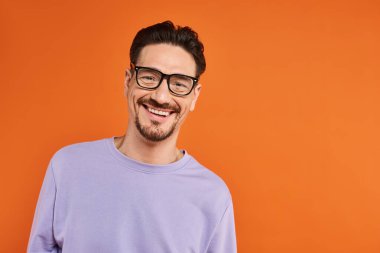 cheerful man in purple sweatshirt and trendy eyeglasses on orange background, positive emotion clipart