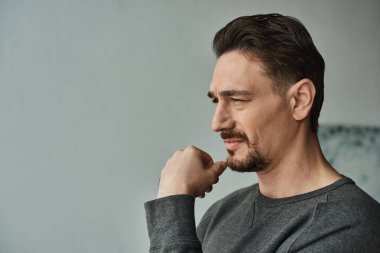 Düşünceli ve sakallı gri kazaklı bir adam evde derin düşüncelere dalmışken gözlerini kaçırıyor.