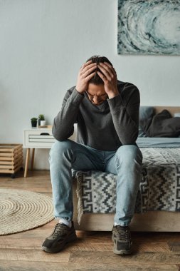 Evde takılan üzgün sakallı adam evde otururken kafasına dokunuyor, depresyonda.