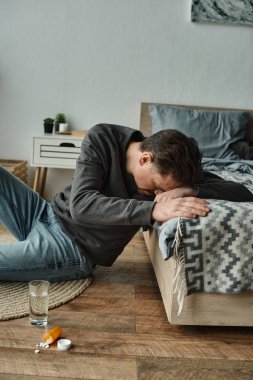 Stresli sakallı adam yatak odasındaki cam su ve ilacın yanında oturuyor, haplar...