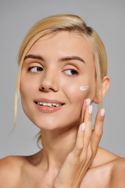 portrait pretty girl in her 20s with healthy skin applying cream on face in grey background clipart