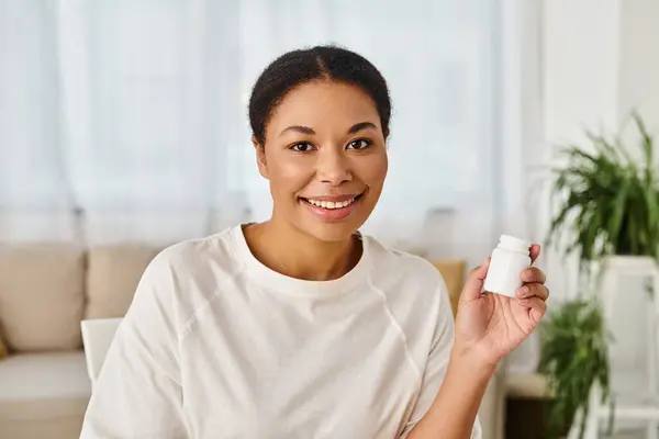 stock image portrait of happy african american nutritionist holding supplements in a bottle for healthy diet