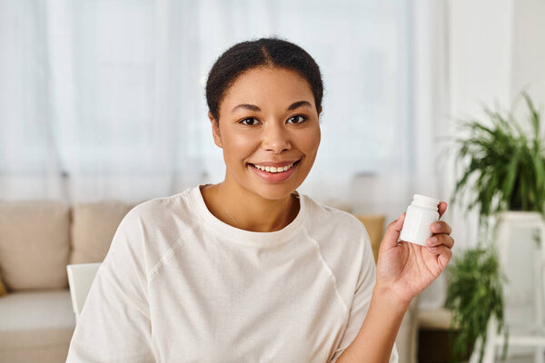 portrait of happy african american nutritionist holding supplements in a bottle for healthy diet