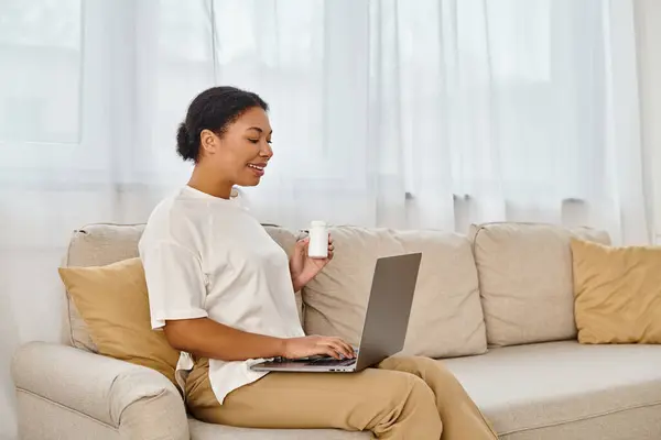 Stock image happy african american nutritionist with supplements giving dietary tip via laptop in living room