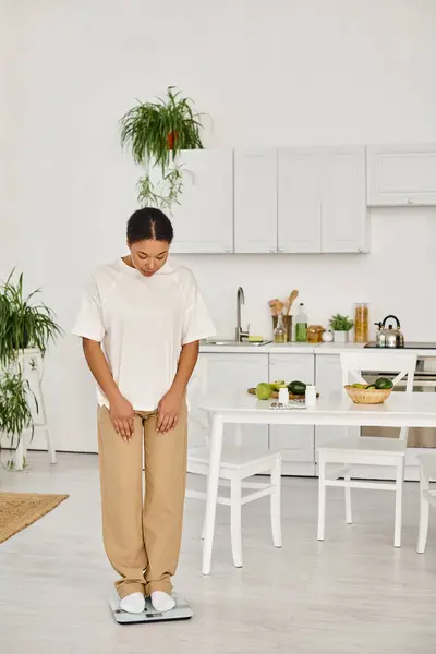 身着休闲装的非洲裔美国妇女站在厨房 体重管理例行公事的尺度上 — 图库照片