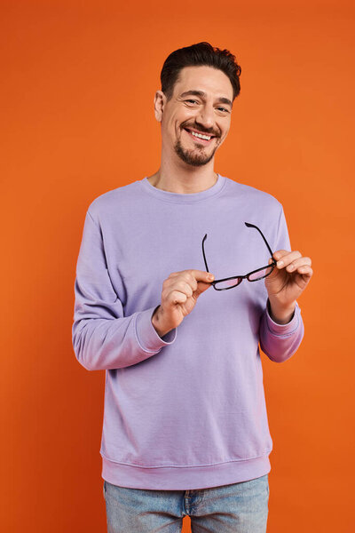 весёлый мужчина в фиолетовой толстовке с очками на оранжевом фоне, позитивные эмоции
