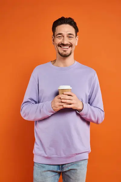 笑容满面的男人拿着装有咖啡的纸杯去享受橙色的背景 — 图库照片