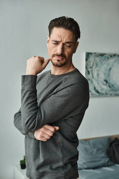 бородатый человек чувствует дискомфорт и боль, стоя дома, мышечное напряжение и проблемы со здоровьем