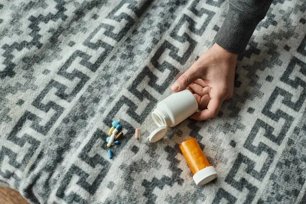 stock image cropped photo of male hand reaching bottle with medication on grey blanket with ornament, pills