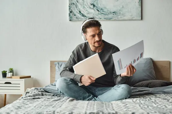stock image bearded man in wireless headphones analyzing graphs and listening music in bedroom, work from home
