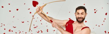 funny bearded cupid man archering under red confetti during st valentines party on grey, banner clipart