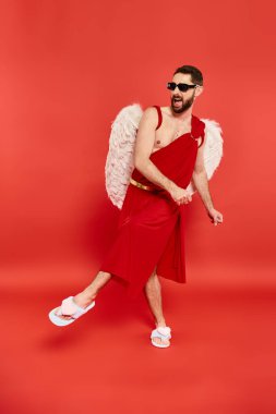 full length of excited bearded man in cupid costume dancing on red, st valentines day celebration clipart