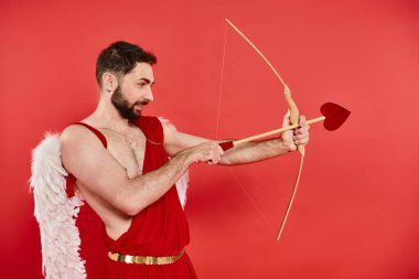 Eros kostümü giymiş sakallı bir adamın yan görüntüsü. Kırmızıya ok şeklinde okçuluk ve nişan alıyor.