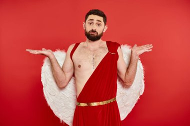 confused bearded man in cupid costume showing shrug gesture and looking at camera on red backdrop clipart