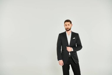 good-looking bearded businessman in black stylish suit standing and looking away on grey backdrop clipart
