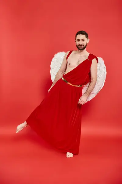 stock image bearded man in cupid costume and wings standing in theatrical pose on red, Saint Valentines day