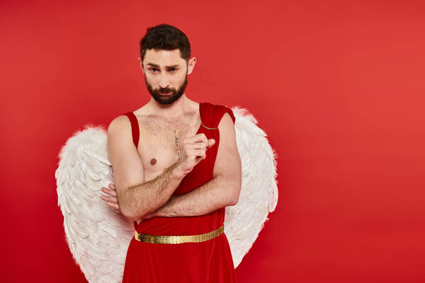 strict serious bearded man in cupid costume showing attention gesture on red, st valentines concept