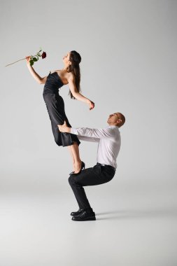 Kırmızı gül giymiş genç bir kadın performans sırasında dansçının kucağında dengede duruyor.