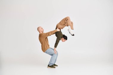 Gri arka planda stüdyoda akrobatik denge sergileyen gündelik kıyafetli sanatçı çift.